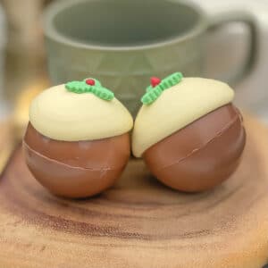 2 hot chocolate christmas pudding bombs in front of a mug